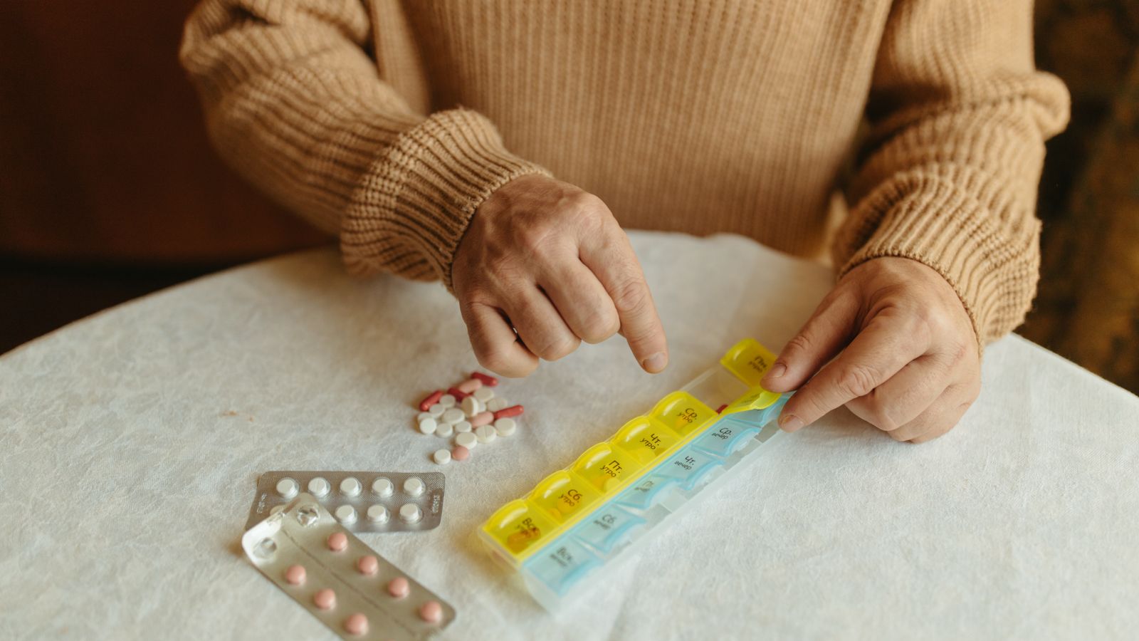 Adulto mayor organizando sus pastillas en un pastillero semanal en casa en Florida